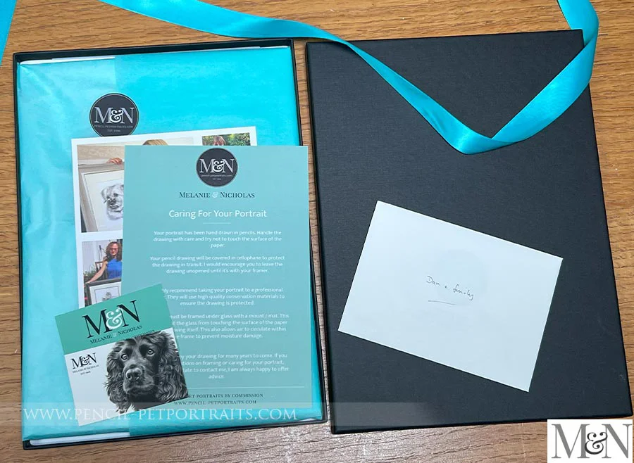 Close-up of a pencil pet portrait being wrapped in tissue paper inside its presentation box.