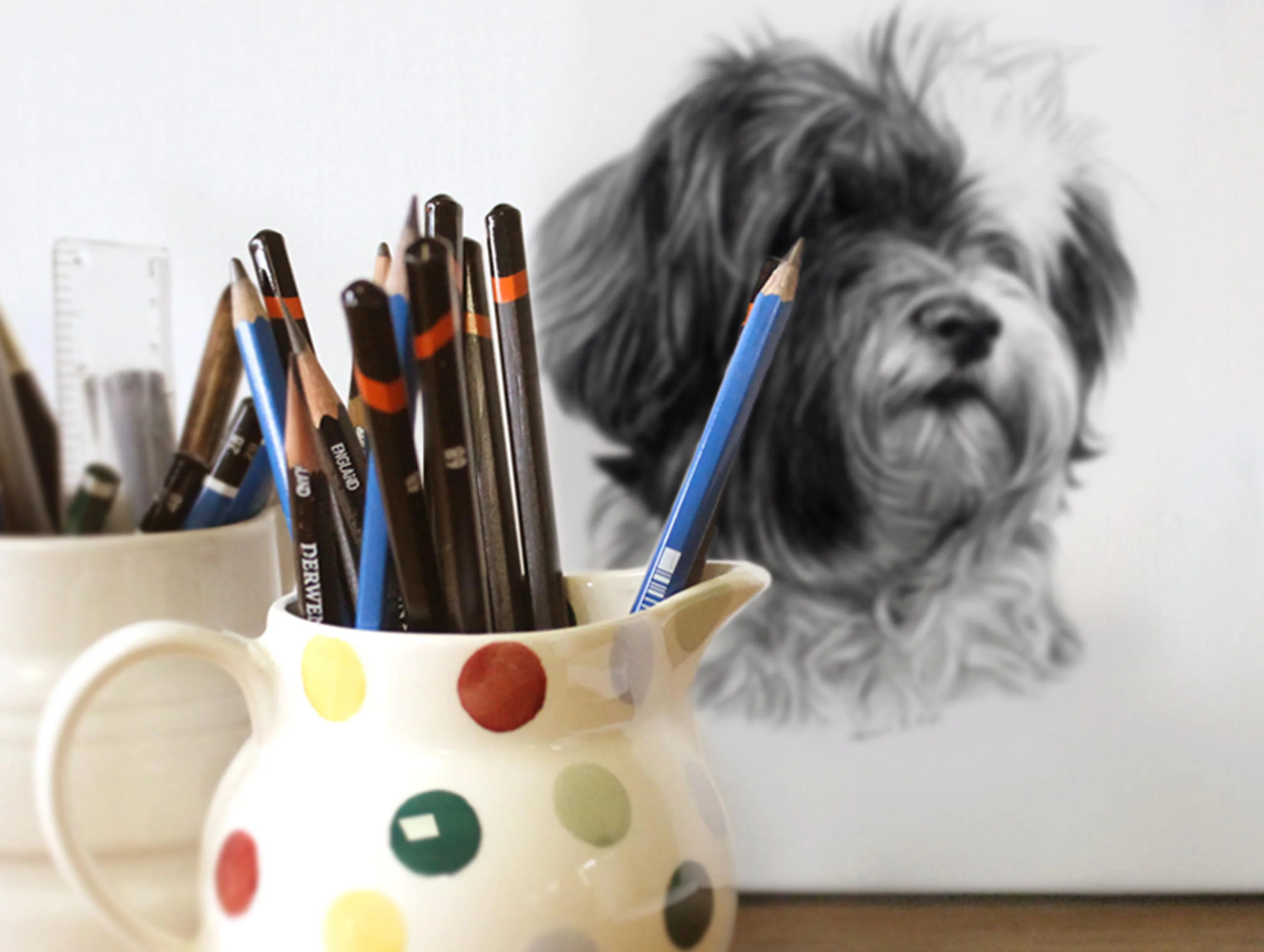 Melanie's graphite pencils (Staedtler, Derwent, Faber Castell) alongside a finished pet portrait.